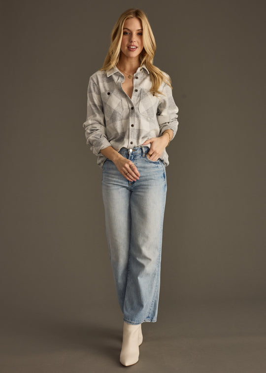 Woman wearing a light gray button-up shirt and blue jeans against a dark background