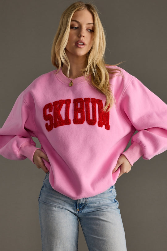 Person wearing a pink sweatshirt with 'Ski Bum' text on a gray background