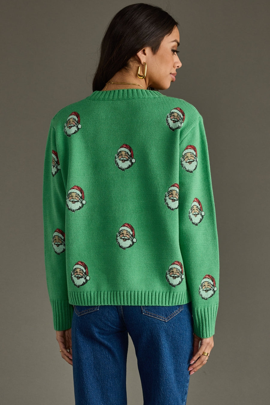 Green sweater with Santa Claus patterns worn by a person on a gray background