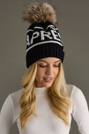 Woman wearing a black knit beanie with a fur pom-pom on a gray background