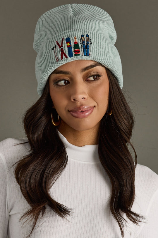 Woman wearing a light blue knit beanie with embroidered designs on a neutral background