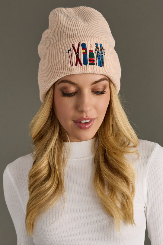 Woman wearing a blush beanie with colorful embroidered designs on a gray background