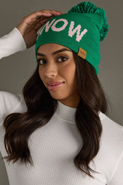 Woman wearing a green beanie with 'NOW' text, posing against a neutral background