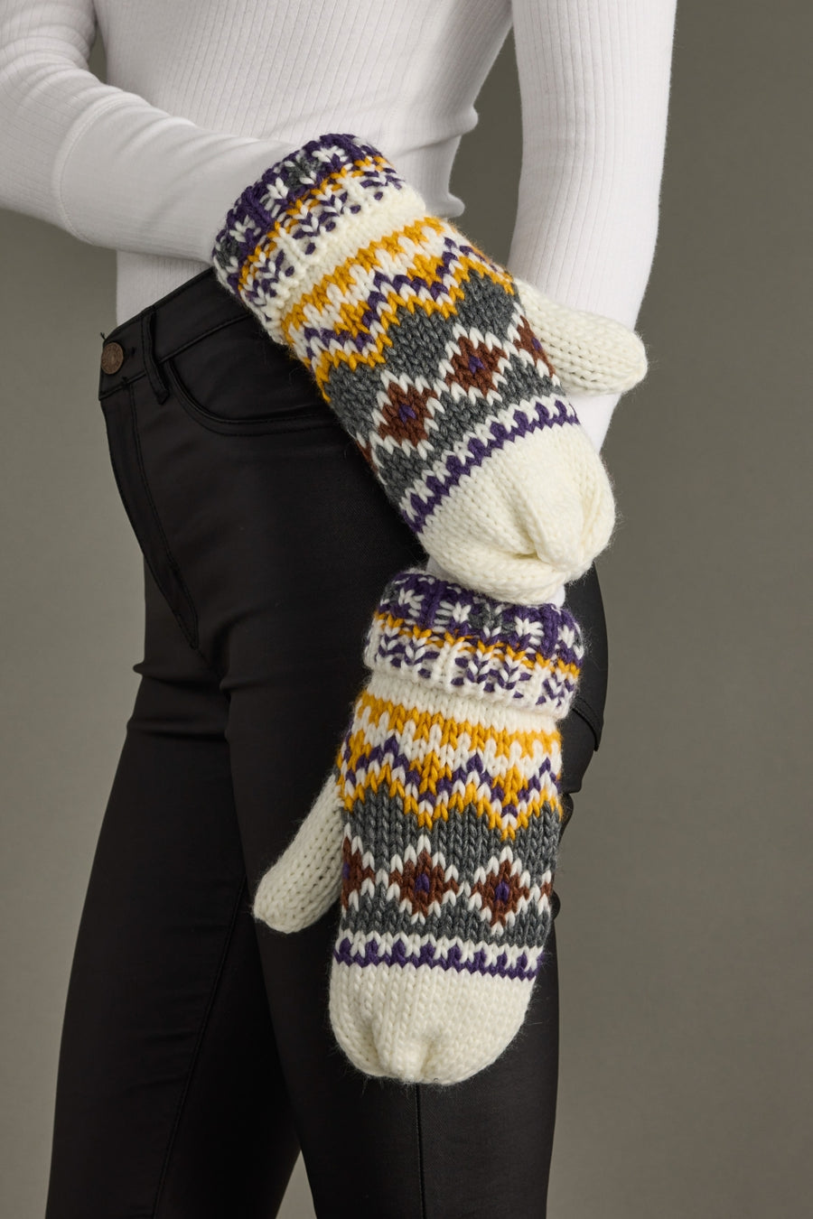 Person wearing a pair of patterned mittens against a neutral background
