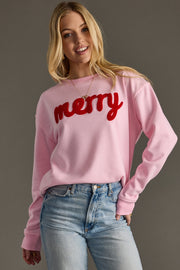 Woman wearing a pink sweatshirt with 'merry' in red text on a gray background