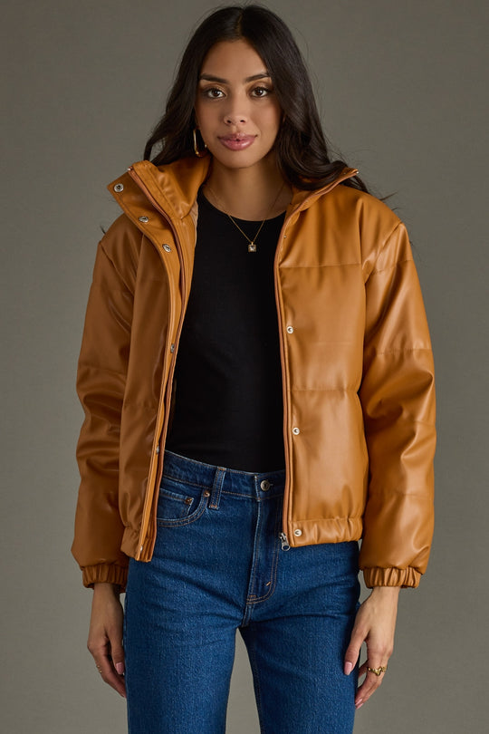 Woman wearing a brown leather jacket over a black top and blue jeans on a gray background