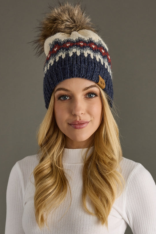 Woman wearing a colorful knit beanie with a pom-pom against a neutral background