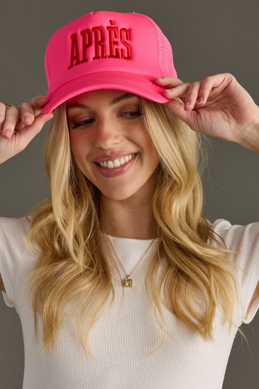 Woman wearing a pink cap with 'APRèS' text, smiling against a gray background