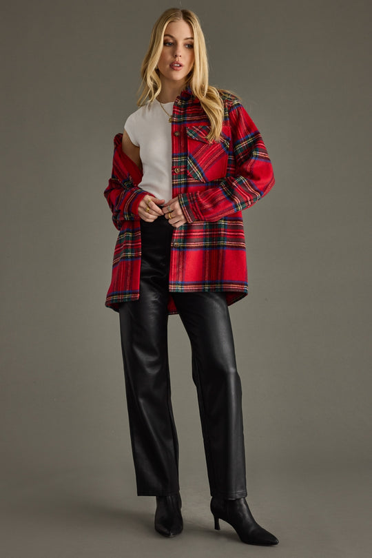 Woman wearing a red plaid coat over a white shirt with black pants on a gray background