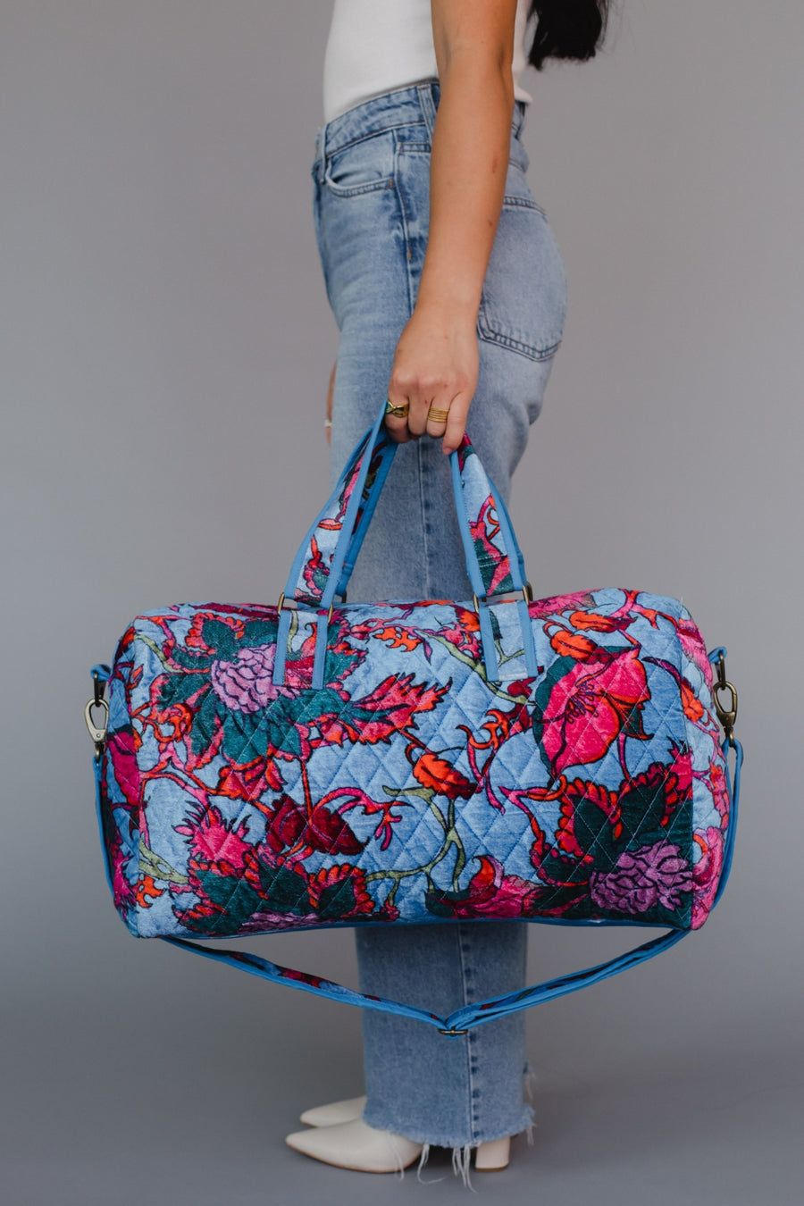 Person holding a floral patterned duffel bag against a gray background