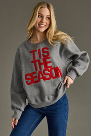 Woman wearing a gray sweatshirt with 'TIS THE SEASON' in red text against a gray background