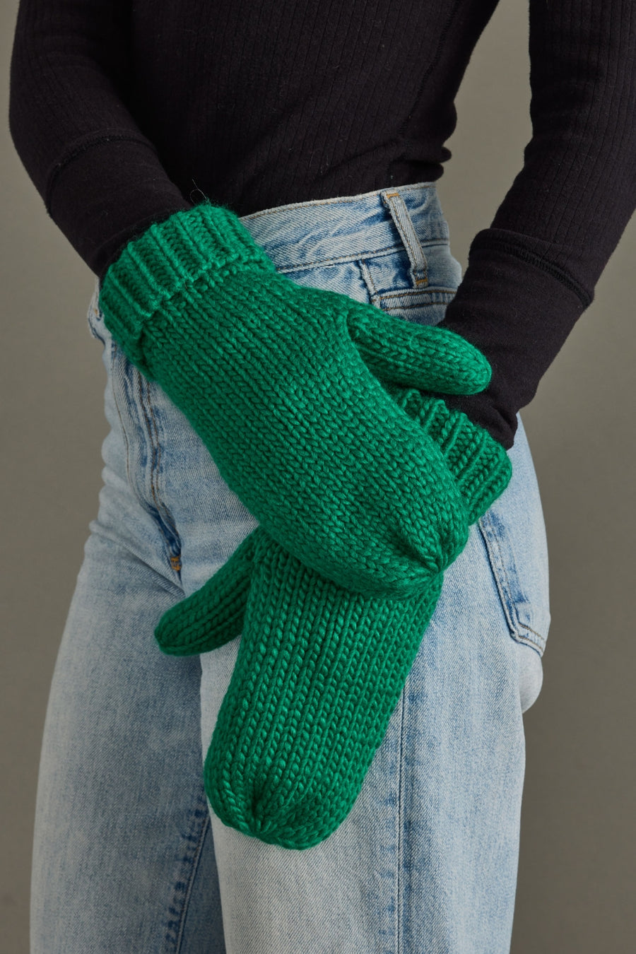 Green knitted gloves worn by a person with a neutral background