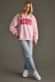 Woman wearing a pink sweatshirt with 'MERRY' text, light blue jeans, and white sneakers on a gray background