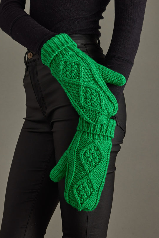 Green knitted gloves held by a person wearing black clothing against a gray background