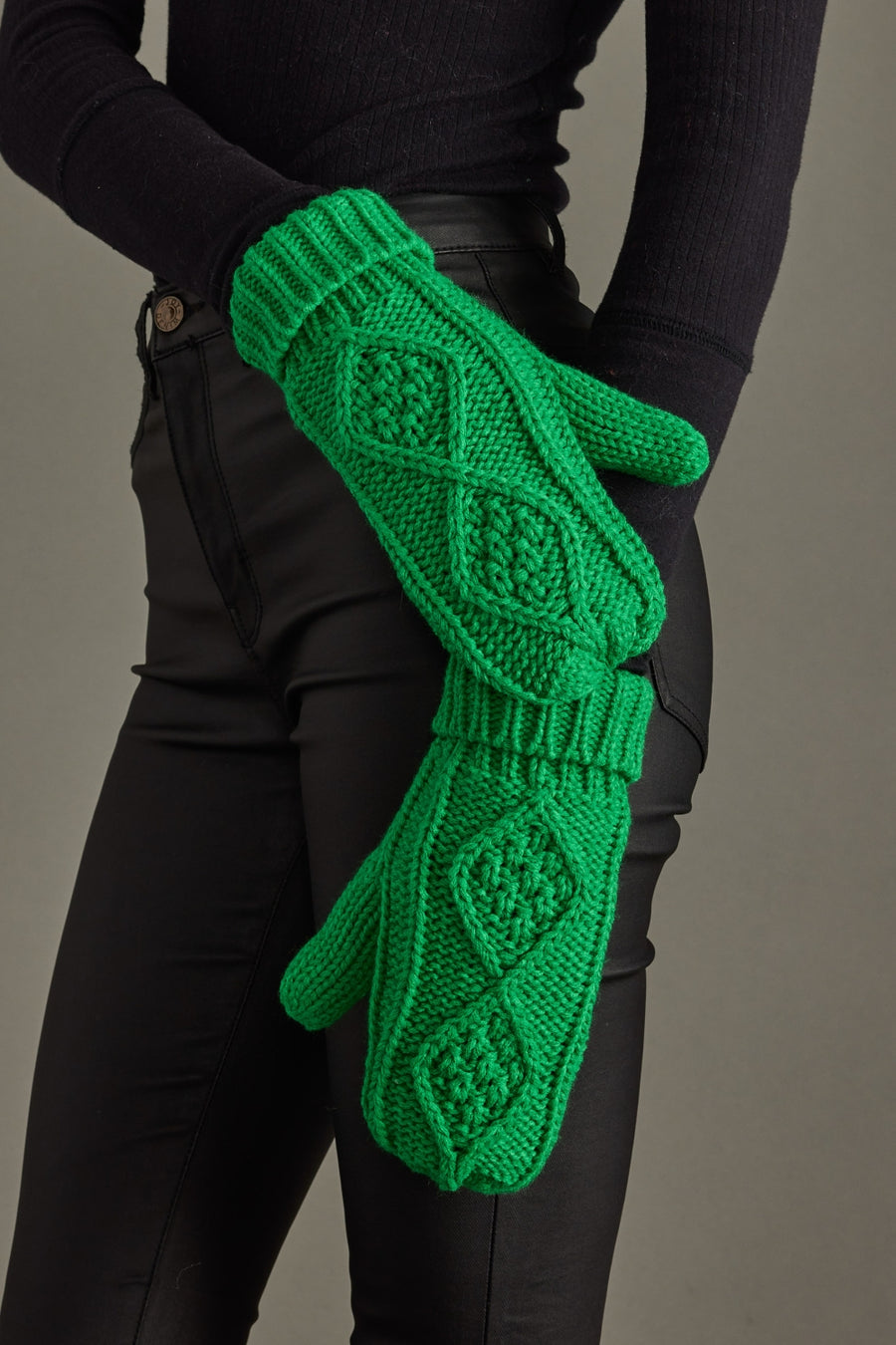 Green knitted gloves held by a person wearing black clothing against a gray background