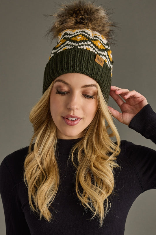 Woman wearing a green beanie with a pom-pom against a gray background