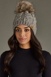Woman wearing a gray knit beanie with a fur pom-pom against a neutral background