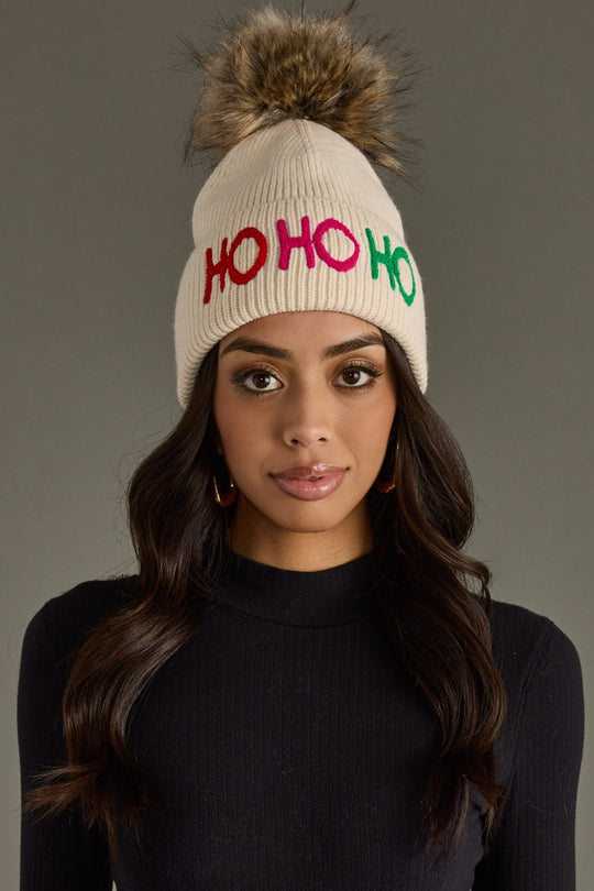 Woman wearing a beige beanie with 'HO HO HO' in colorful letters on a gray background