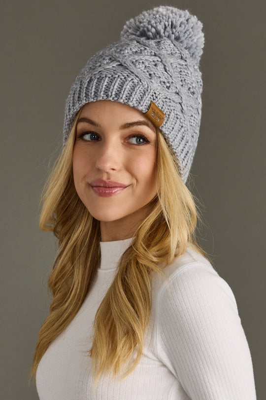 Woman wearing a gray knit beanie with a pom-pom on a brown background