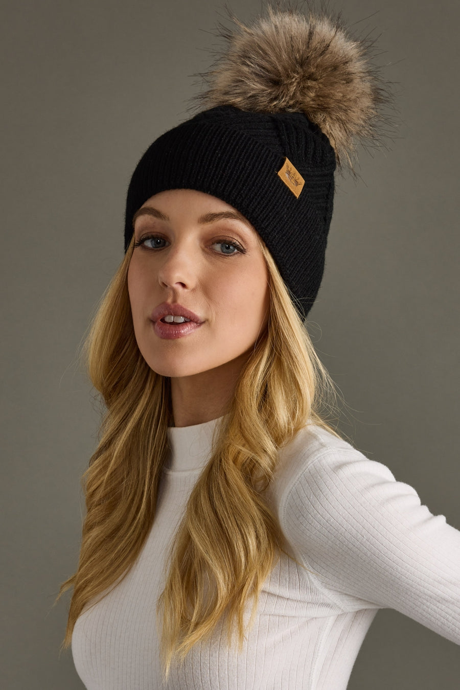 Woman wearing a black knit beanie with a fur pom-pom on a gray background