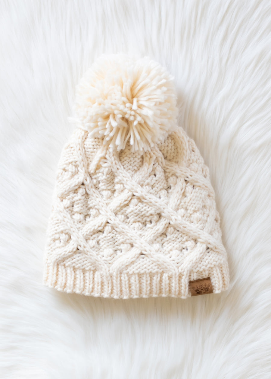 Knitted cream beanie with a pom-pom on a white background