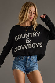 Woman wearing a black sweater with 'COUNTRY & COWBOYS' text and denim shorts on a gray background