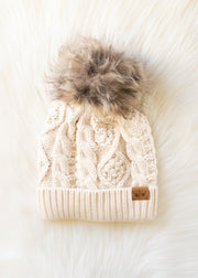 Beige knitted beanie with a fur pom-pom on a white background