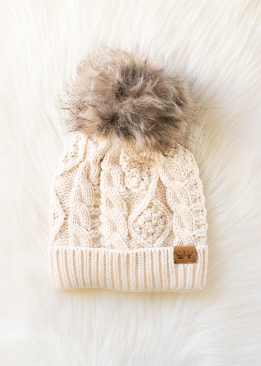 Beige knitted beanie with a fur pom-pom on a white background
