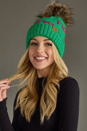 Woman wearing a green beanie with a fur pom-pom against a gray background