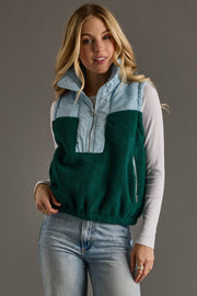 Woman wearing a green and light blue two-tone vest against a gray background