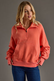 Woman wearing a coral pink pullover with a zipper on a gray background