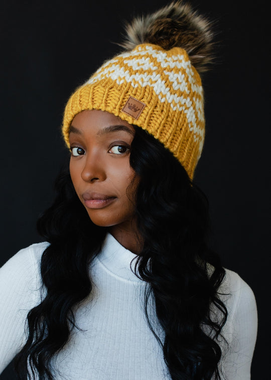 Woman wearing a yellow knit beanie with a pom-pom against a black background