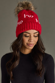 Woman wearing a red beanie with a fur pom-pom on a gray background