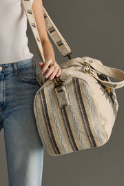 Person holding a beige handbag with striped pattern against a gray background