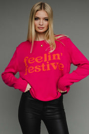 Woman wearing a bright pink sweater with 'feelin' festive' text on a gray background