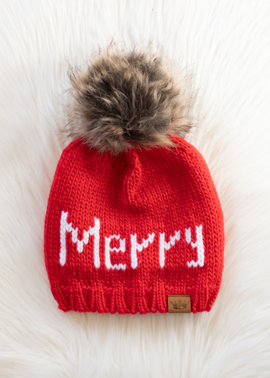 Red knit hat with 'Merry' text and fur pom-pom on a white background