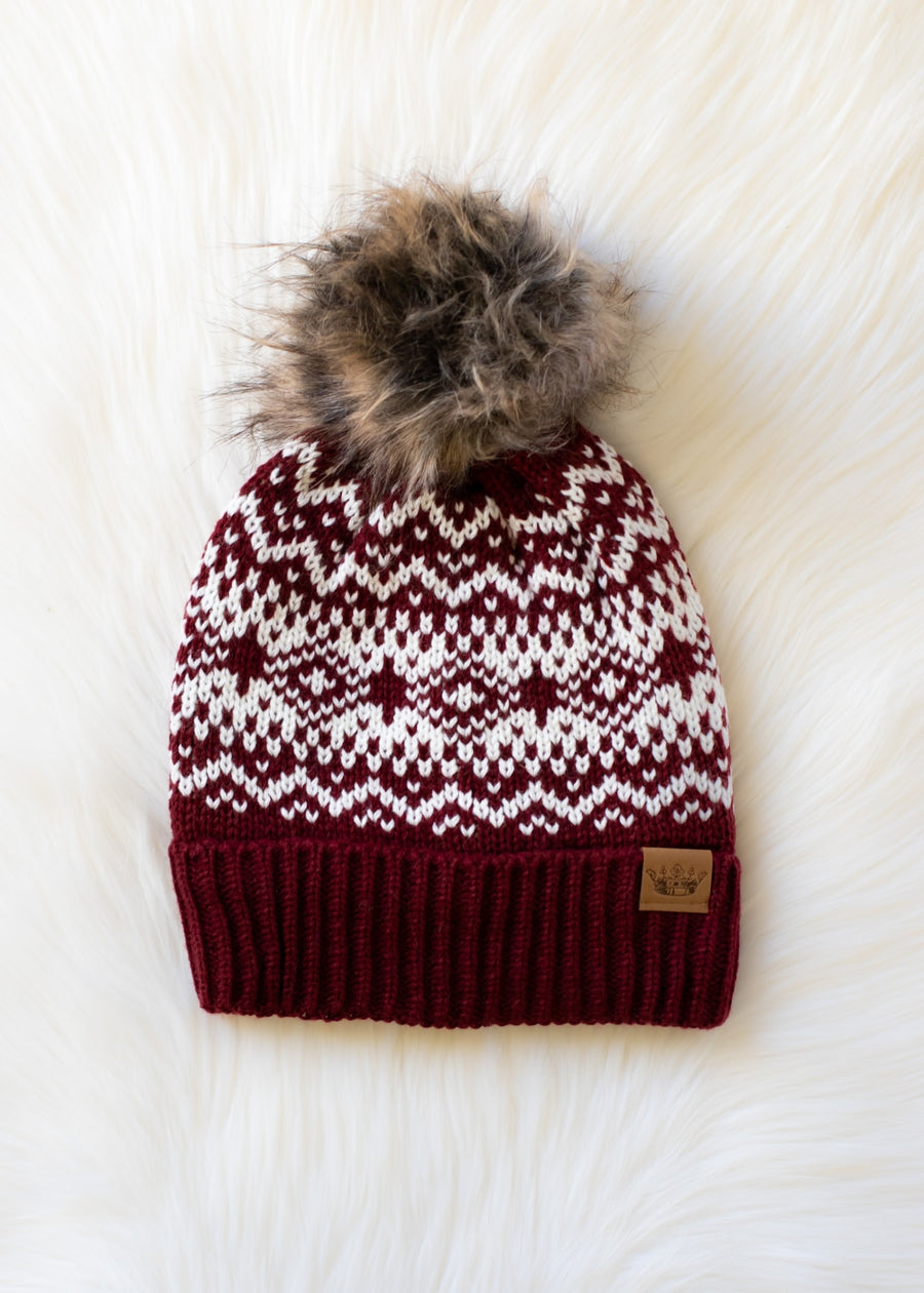Knitted beanie with a pattern and fur pom-pom on a white textured background