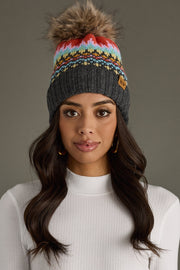 Woman wearing a colorful knit beanie with a pom-pom against a gray background