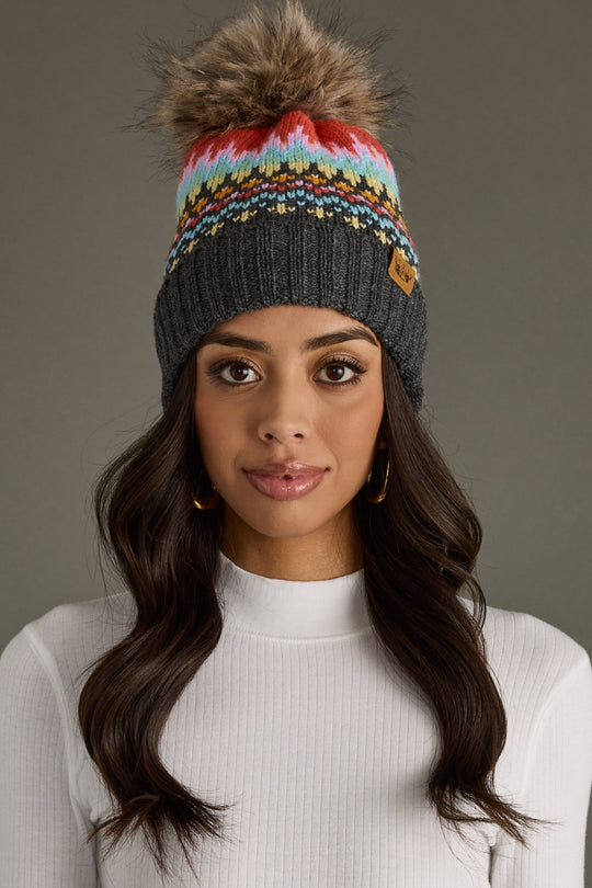 Woman wearing a colorful knit beanie with a pom-pom against a gray background