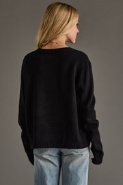 Person wearing a black sweater and light blue jeans against a gray background