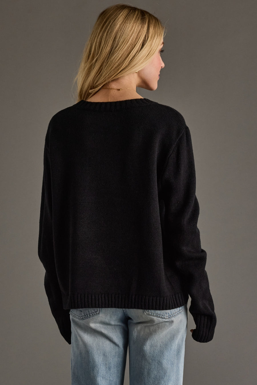 Person wearing a black sweater and light blue jeans against a gray background