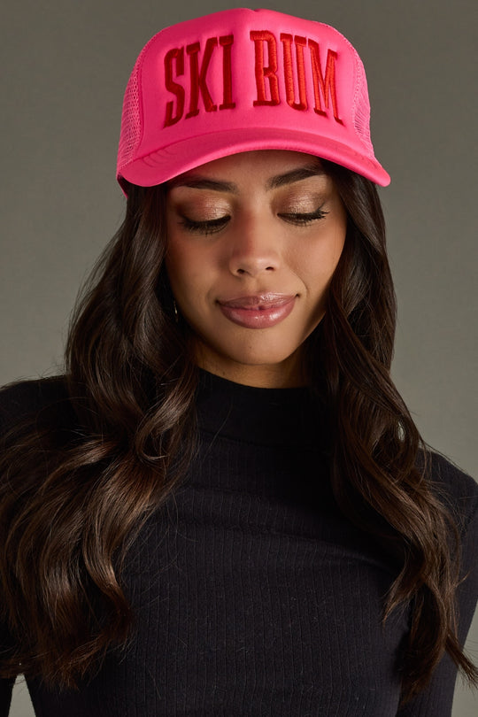 Woman wearing a pink cap with 'SKI BUM' text against a gray background