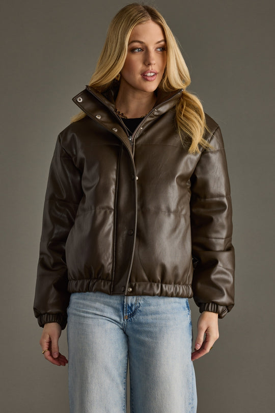 Woman wearing a brown jacket and blue jeans against a gray background