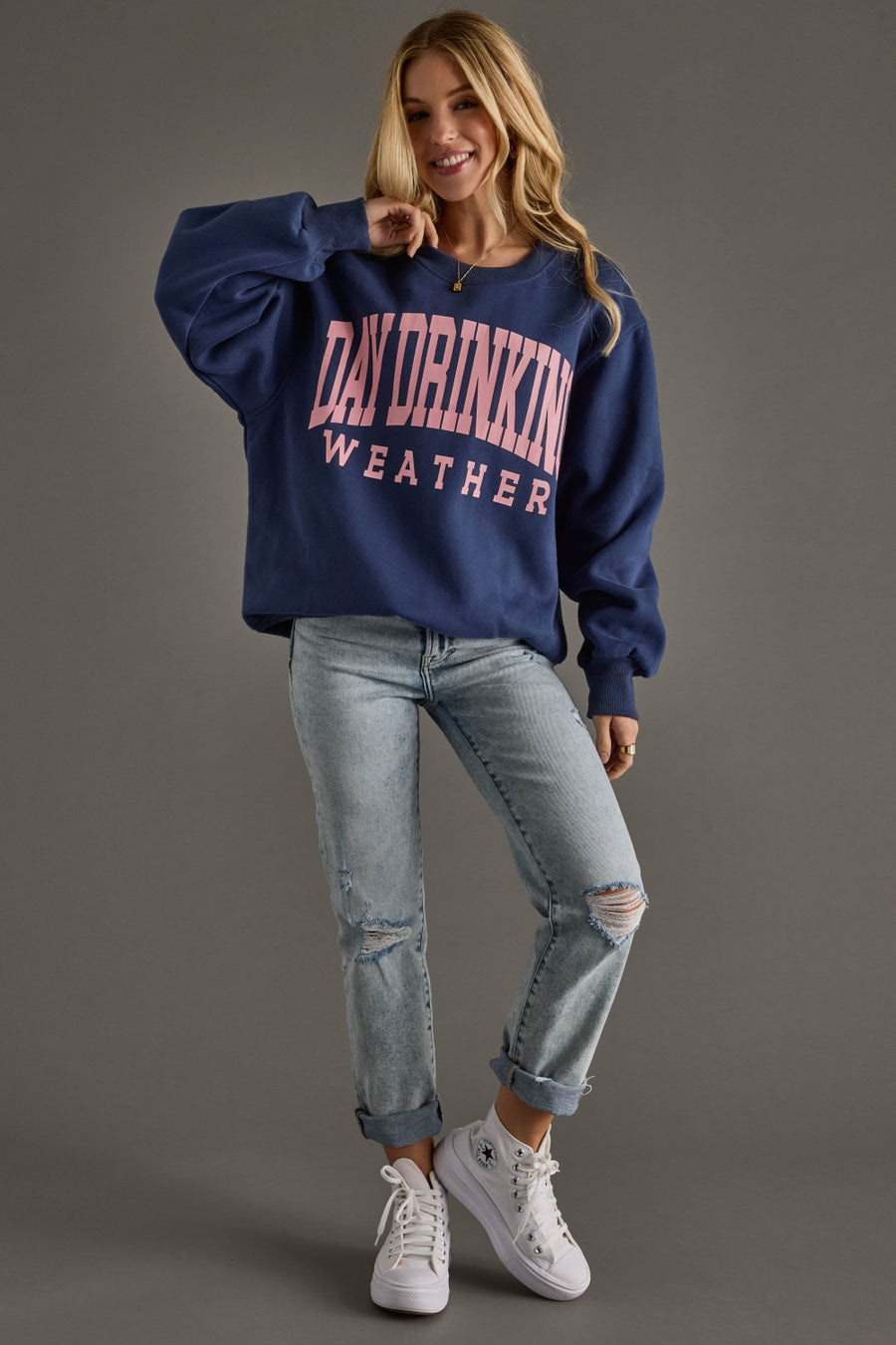 Woman wearing a navy sweatshirt with text, light blue jeans, and white sneakers on a gray background