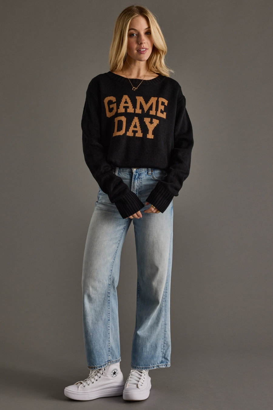 Person wearing a black 'GAME DAY' sweater with light blue jeans on a gray background