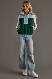 A woman stands against a gray background wearing the Panache Apparel Collection Light Blue & Green Vest over a light blue long-sleeve shirt, paired with light blue jeans and white sneakers, with her hands in her vest pockets.
