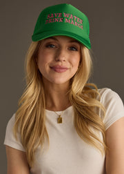She’s rocking a bright green trucker hat with bold pink lettering that reads **“SAVE WATER DRINK MARGS.”** Paired with loose waves, a simple white tee, and a gold pendant necklace, the whole look is fun, flirty, and very “ready for happy hour.”
