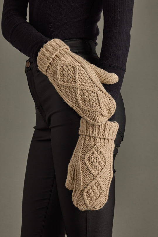Beige knitted gloves with intricate patterns worn by a person against a neutral background