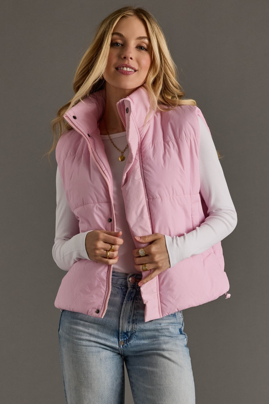 Woman wearing a pink puffer vest over a white shirt with a gray background