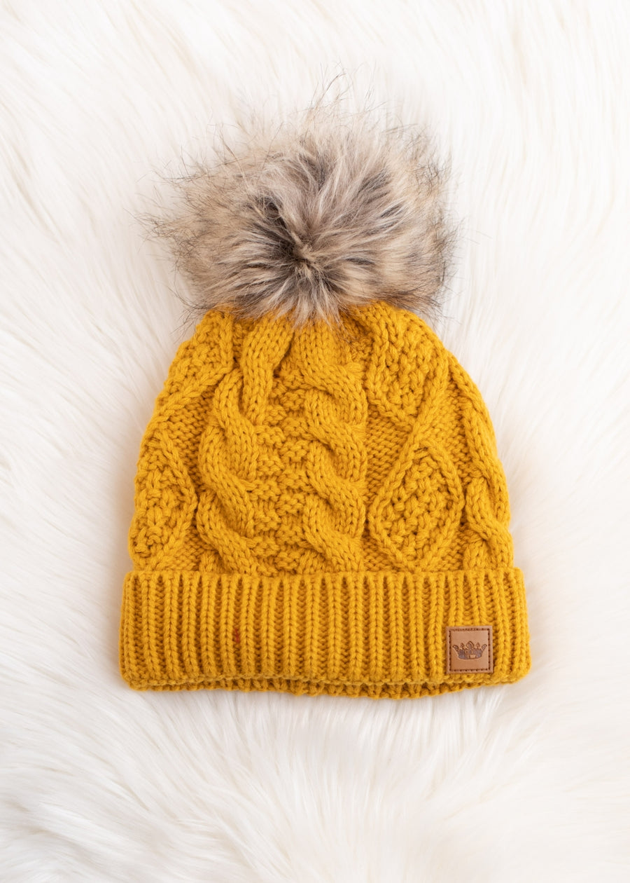 Mustard yellow knit beanie with a fur pom-pom on a white background